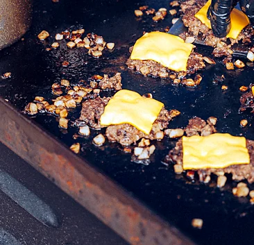 Burger patties smashed on the griddle with melting cheese
