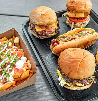 Smash burgers, a hot dog and loaded fries on a tray