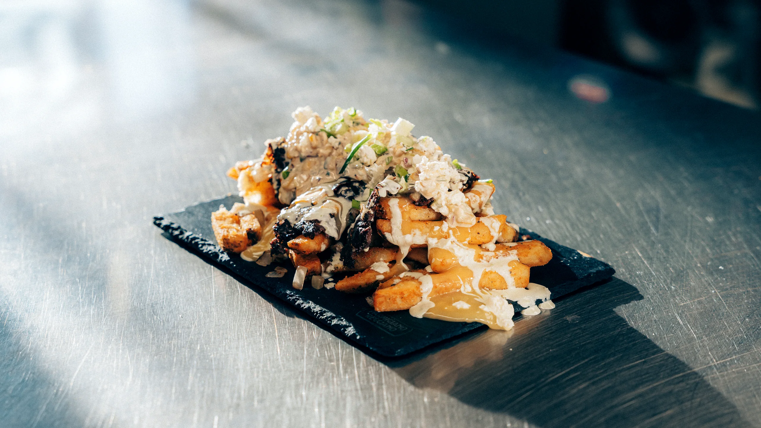 Loaded fries with cheese sauce and green onion on a slate board