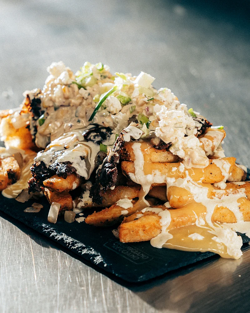 Loaded fries with cheese sauce and green onion on a slate board